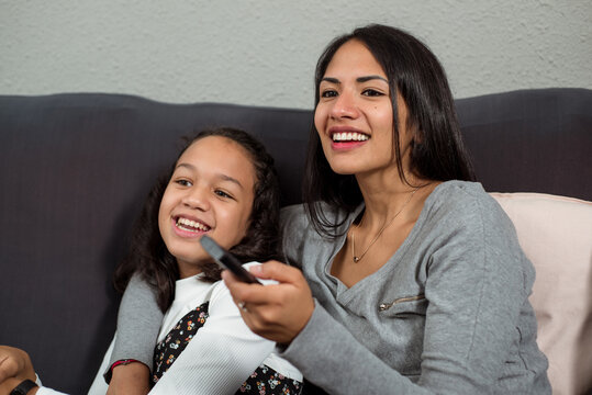 Latin mother and daughter laughing watching series on television.