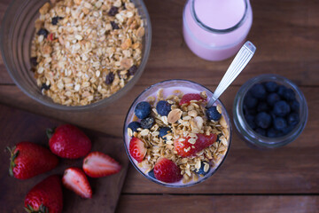 glass with yogurt, cereals, strawberries and blueberries on wooden table - top