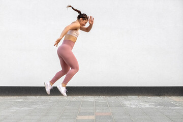 Young fitness girl in training sportswear jump high in jogging exercise outside on street.