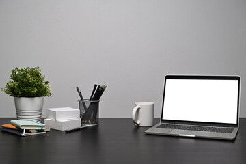 Computer laptop with blank display, coffee cup and supplies on black table.