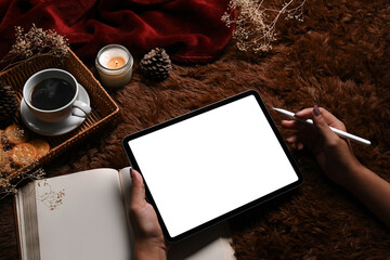 Woman holding stylus pen and using digital tablet on brown carpet.