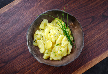 Traditioneller deutscher Kartoffelsalat mit Zwiebel und Schnittlauch serviert als Draufsicht in einer rustikalen Design Schale auf einem Holz Board mit Textfreiraum