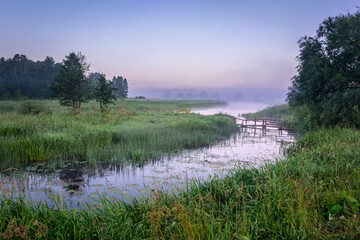 Landscape of early morning summer mist over the river with a view of the old destroyed bridge in the distance.