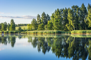 Obraz premium Beautiful sunny landscape with forest reflection in the pond. Belarusian rural landscape.