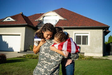 Soldier in uniform coming home and his lovely family with American flag running into his arms celebrating reunion.