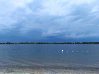 Clouds over the lake, beautiful lake and gloomy sky. Sunny day, the beginning of a thunderstorm.