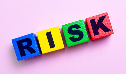 On a light pink background, multi-colored wooden cubes with the text RISK.