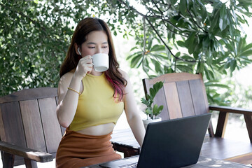 Beautiful asian girl, Work from home by communicating through social media. In the era of COVID19, Working from home is important. Social distancing, Wearing a mask. A young woman working in  garden