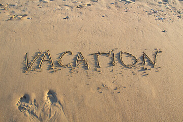 Word VACATION wrote on the sand against background. Message says 