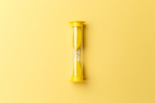 Modern yellow Hourglass with yellow background. Sand trickling through the bulbs of a crystal sand glass. Symbol of time. Countdown. Copy space. Top view. Concept