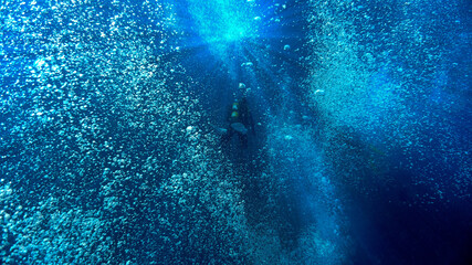 Artistic underwater photo of a scuba diver floating in a dream of air bubbles and rays of light in the deep blue ocean.