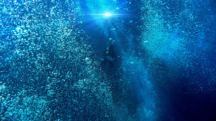 Artistic underwater photo of a scuba diver floating in a dream of air bubbles and rays of light in...