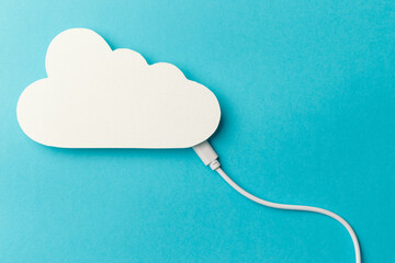 The concept of cloud technologies, cloud storage. A white cable is connected to a cloud on a blue background. Top view. Flat lay. Close-up. Copy space. Transferring data to cloud storage