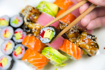 Man takes Tasty Colorful assorted Set of different type Sushi with chopsticks. Dinner in Japanese style. Healthy food. Filadelfia and Maki sushi rolls with Avocado, Tuna, Salmon, fish and Prawns.