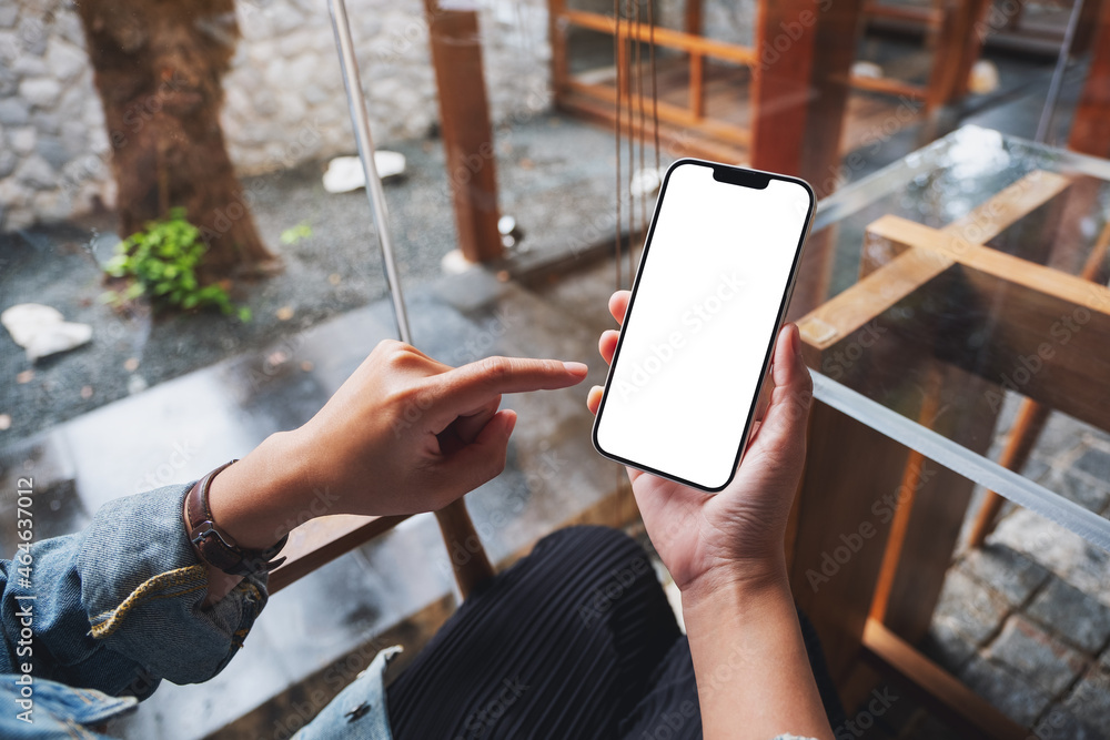 Wall mural mockup image of a woman holding and pointing finger at mobile phone with blank white desktop screen 