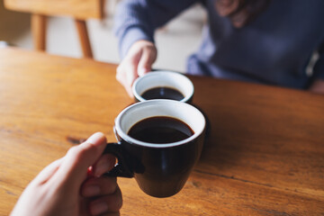 Closeup image of a man and a woman clinking coffee mugs in cafe