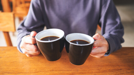 Closeup image of a woman holding and clinking two cups of coffee