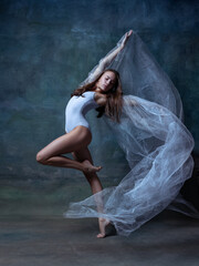 Portrait of young and flexible ballet dancer, ballerina dancing isolated on dark vintage studio...