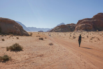 Fototapeta na wymiar A girl walks on an empty road in the Wadi Rum desert, a clear cloudless day, Jordan
