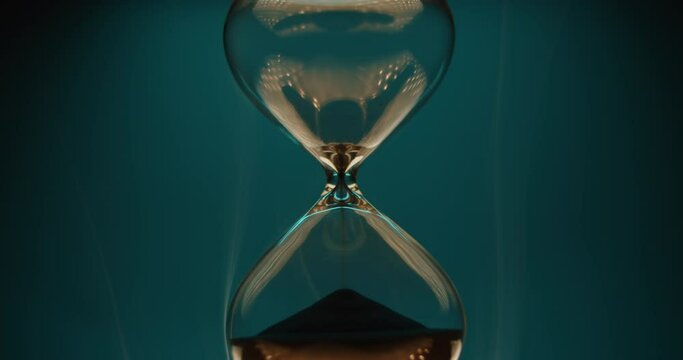 Beautiful smoke surrounding an hourglass with black sand on turquoise background. Abstract time concept. 