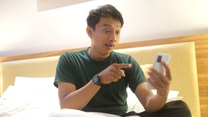 Shocked Asian man seeing chat news on smartphone in bedroom