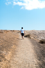 Young traveler walking along a mountain road during a sunny day. Hiker walking with copy space top.