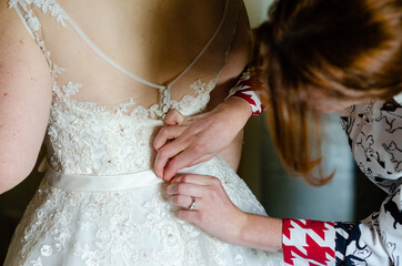 Bride preparing for the ceremony - wedding dress being buttoned up from behind by bridesmaid - closeup