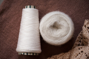 spool of silk yarn and a skein of light fluffy yarn on a brown background. materials for knitting and needlework. handmade.