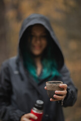 beautiful woman with blue hair and in a raincoat holds out a cup of tea