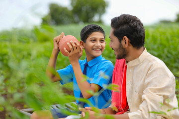 importance of saving concept : Smart indian little boy standing and holding piggy bank in hand at agriculture field.