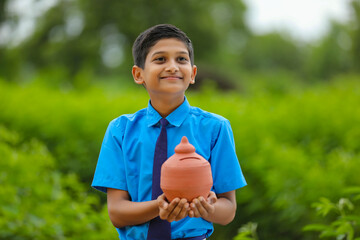 importance of saving concept : Smart indian little boy standing and holding piggy bank in hand at...