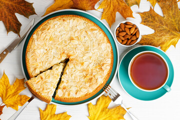 Homemade berry pie decorated with almond petals and cup of tea on white wooden table. Top view.
