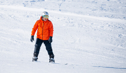 A snowboarder in a ski resort rides on a slope of snow-capped mountains. Winter kind of leisure,...
