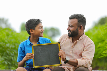 education concept : young indian farmer showing blank chalkboard with his child - obrazy, fototapety, plakaty