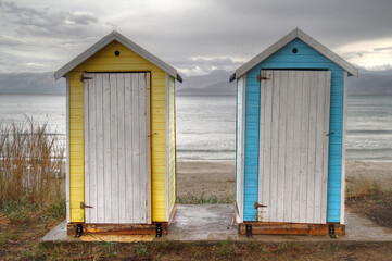 Two small blue and yellow portable toilet houses on the beach on a dark, drizzly day