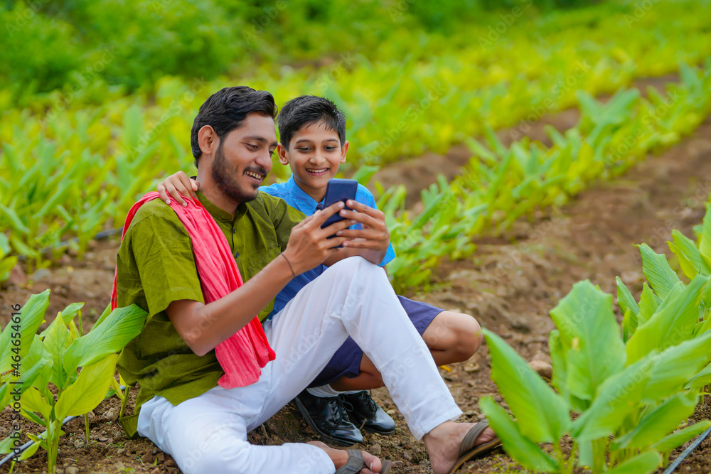 Canvas Prints Indian farmer using smartphone with his child at green turmeric agriculture field.