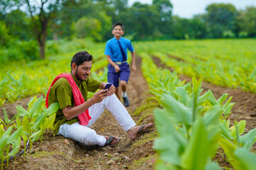 Naklejka na ściany i meble Indian farmer using smartphone with his child at green turmeric agriculture field.