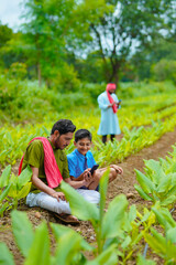 Fototapeta premium Indian farmer using smartphone with his child at green turmeric agriculture field.