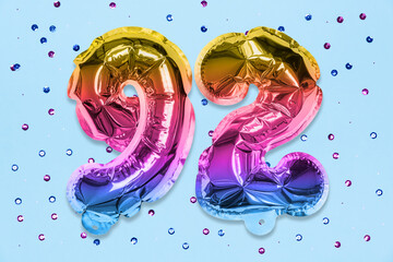 Rainbow foil balloon number, digit ninety two on a blue background with sequins. Birthday greeting...