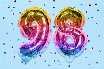 Rainbow foil balloon number, digit ninety eight on a blue background with sequins. Birthday greeting card with inscription 98. Top view. Numerical digit. Celebration event, template.