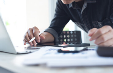 Asian business man working at office with laptop computer and digital tablet and financial report graph data documents on his desk, close up