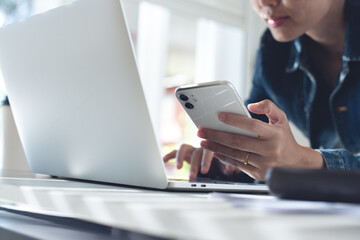 Young asian business woman working on laptop computer and using mobile phone at home office, close up
