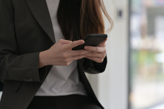 Cropped image of young woman hands using a smartphone over blur office background.