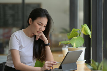 Photo of beautiful woman keep a hand on chin while using a digital tablet and stylus pen at the...