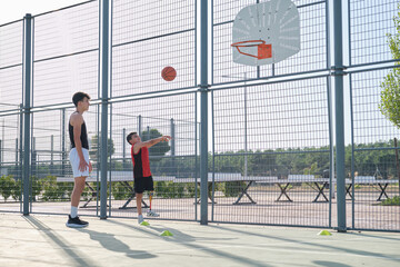 Brother teach how to shoot a basketball to his sibling with a prosthesis.