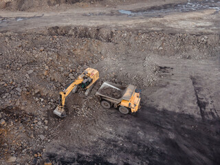 the excavator loads the earth into the truck, digs the earth, large machinery. a flying drone. top view
