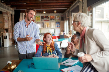 An elderly female boss in the office is chatting with her young colleagues while working together