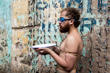 Man performs protest performance at the Sao Joaquim fair in Salvador. He is shirtless, holds a white basin of water, and wears diving goggles.