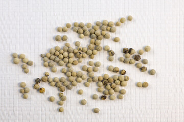 Spices, white peppers, pepper seeds sprinkled on white textured background, close-up