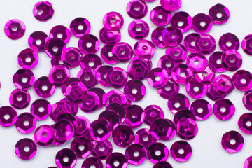 Bright beautiful purple sparkles sequins scattered on white textured background, close up macro